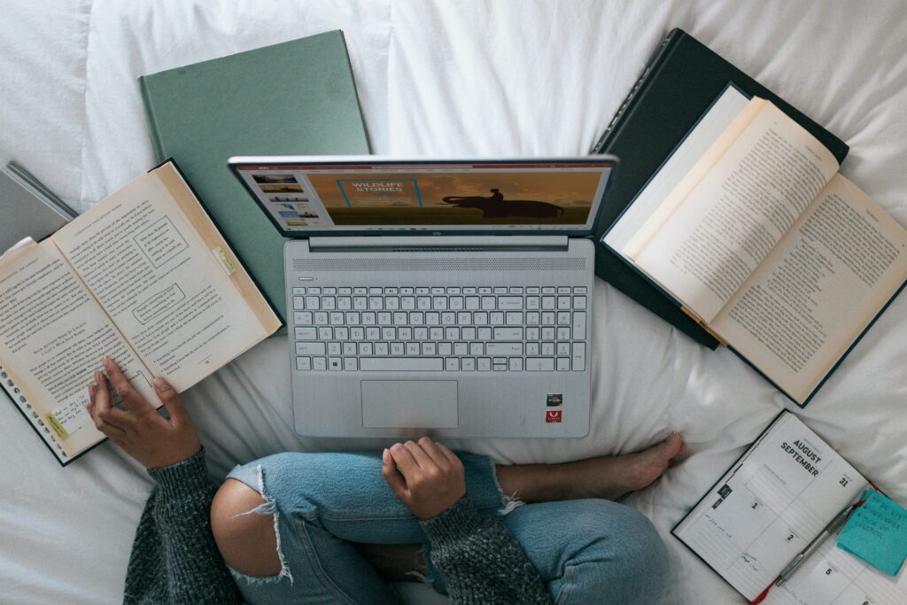 a person studying on bed with books and computer