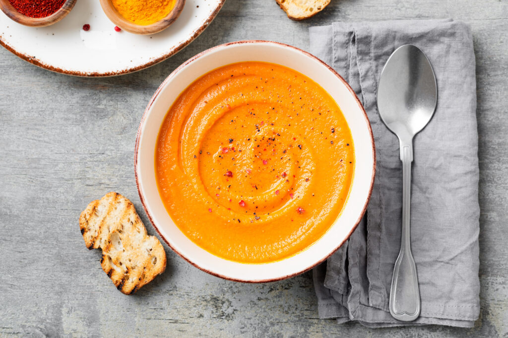 Holiday pumpkin and carrot soup with spices on on grey stone background. A colorful, vegetarian soup.