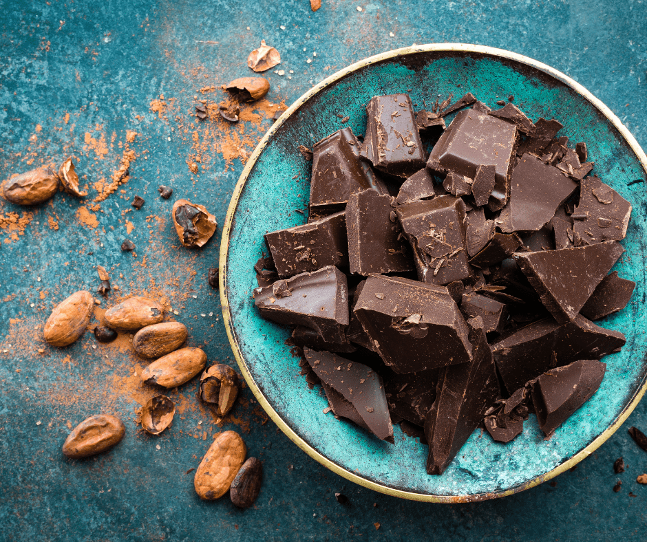 vegan dark chocolate in a blue bowl with cocoa beans to the left of the bowl