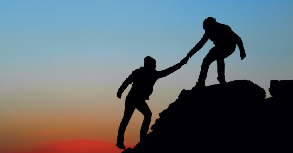 someone helping another person climb a mountain