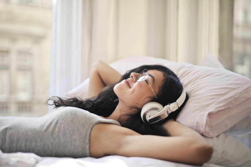 Woman reducing stress by relaxing on a bed with headphones on