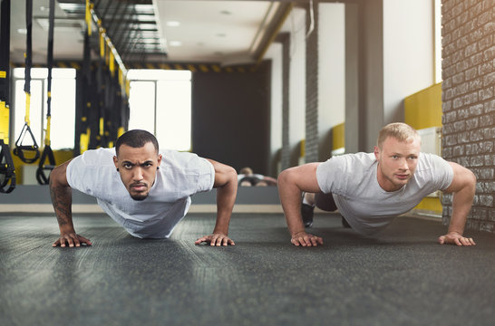 Two friends that are focused doing push ups at the gym.