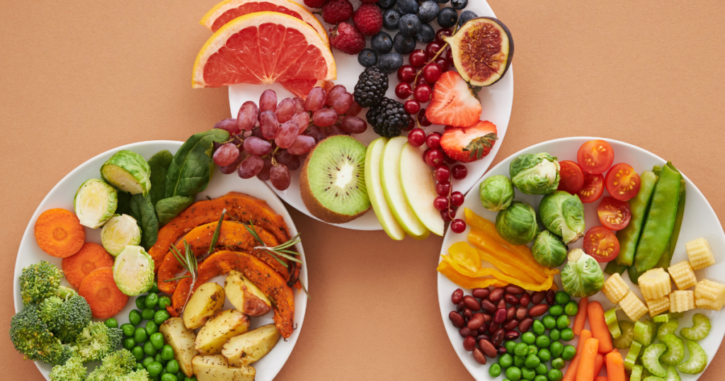 three plates of fresh vegetables and fruits with a tan backdrop for vegetarian