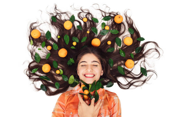 young beautiful cheerful girl lies on floor with her loose hair in mandarins and calamondins. isolated on white. natural skin and hair care products concept