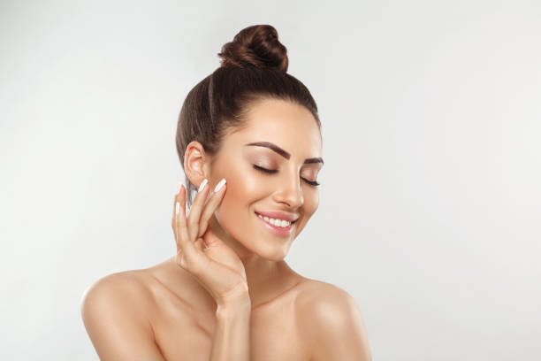 Beautiful young woman with clean perfect skin. Portrait of beauty model with natural nude make up and touching her face. Spa, skincare and wellness. 