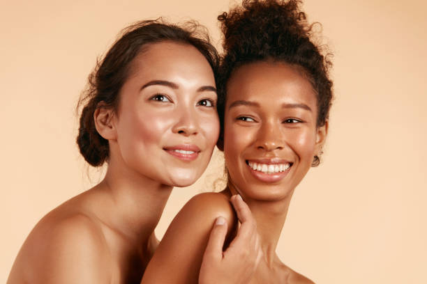 Beauty. Smiling women with perfect face skin and natural makeup portrait. Beautiful happy asian and african girl models with different types of skin on beige background. Spa skin care concept. Natural and Healthy Makeup