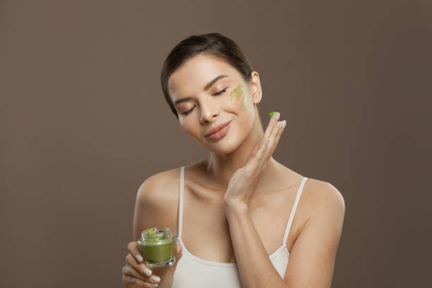 Cute young woman with green face cream mask. Facial treatment and skin care concept