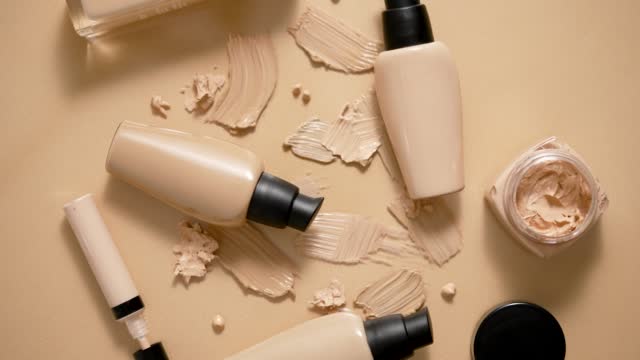 Bottles of makeup foundation and samples on beige background. Flat lay, top view