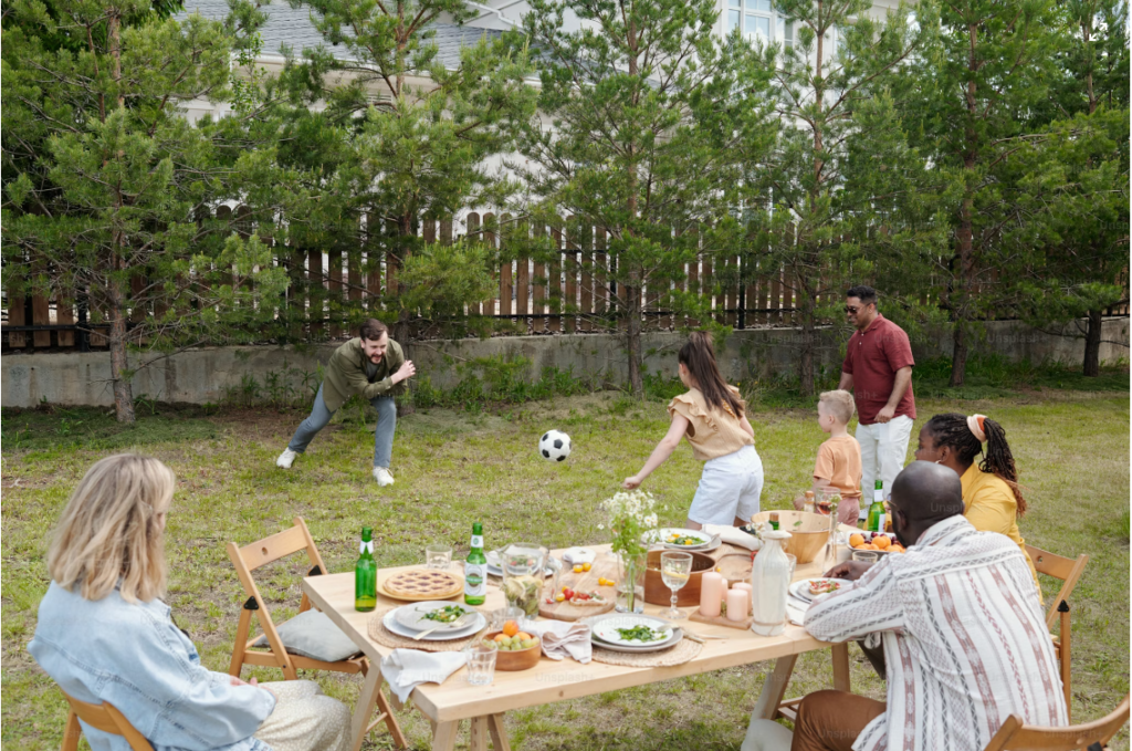Families enjoying outdoor picnic in backyard with people playing with soccer ball 