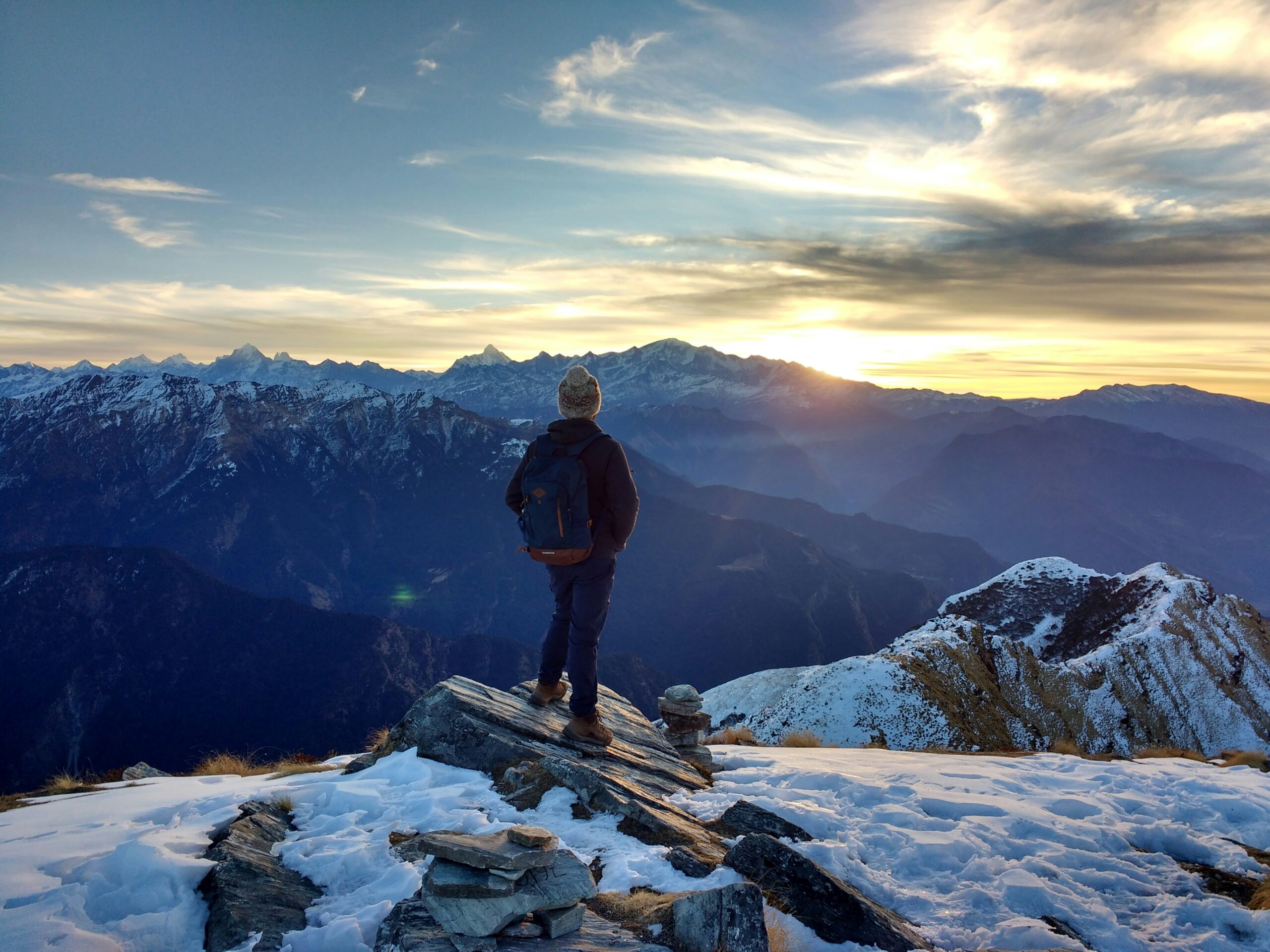 Man with backpack standing on high mountain peak that has snow on the ground
