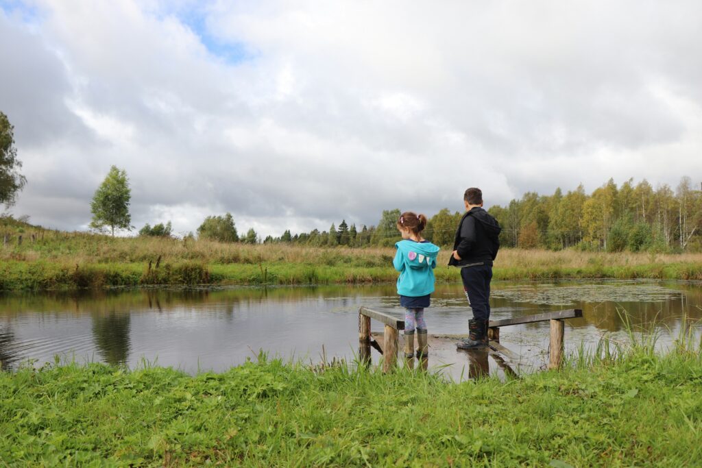 Two kids going outdoors standing on mini port at a pond