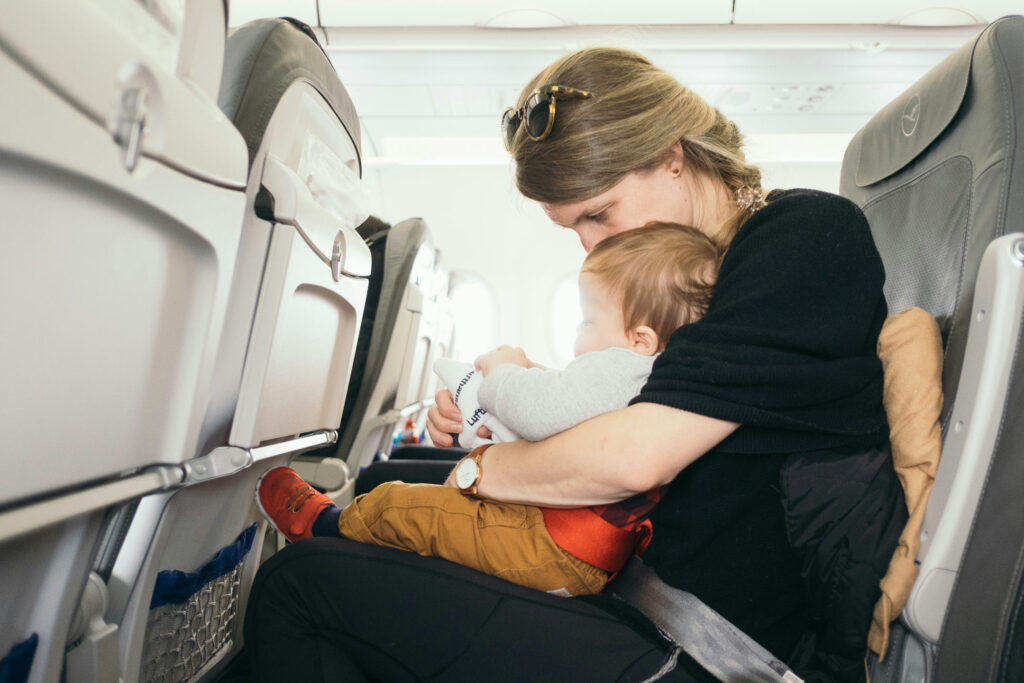 A mother cuddling a toddler on her lap in an airplane seat.