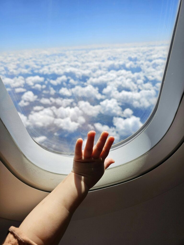 A toddler's hand resting on an airplane window overlooking clouds.