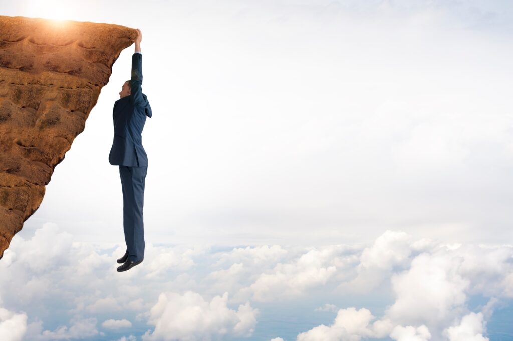 Resilient business man hanging on cliff