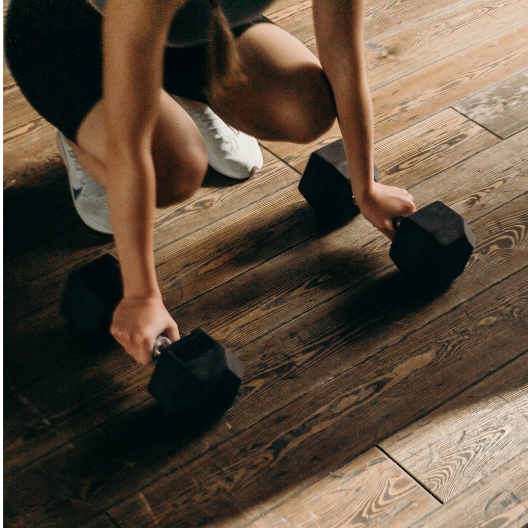 person kneeling with 15 pound weights on a wooden floor ready to workout